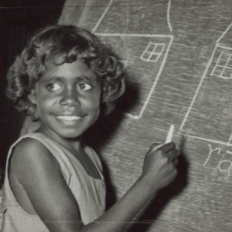 A child is drawing simple house shapes with windows on a chalkboard using a piece of chalk
